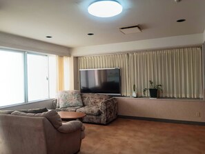 A living room with a sofa, armchair, and a flat-screen TV on a stand. - HotelSumi (Naha)