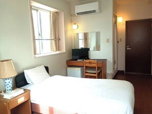 A hotel room with a bed, desk, chair, lamp, air conditioning unit, and a door. - HotelSumi (Naha)