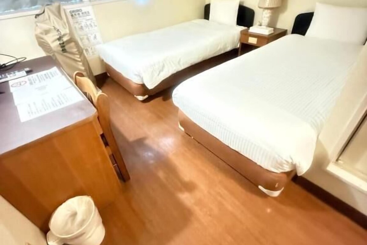 Une chambre d’hôtel avec deux lits simples, un bureau avec un téléphone, une lampe et une fenêtre avec des rideaux.