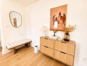 Une pièce comprenant un banc, un meuble orné d’objets décoratifs, un miroir et un tableau accroché au mur.