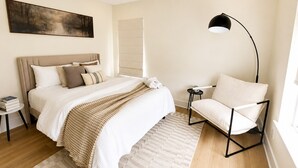 A bedroom with a bed, bedside tables, a chair, a floor lamp, and a painting on the wall. - Muse Atelier | Midtown Houston (Houston)