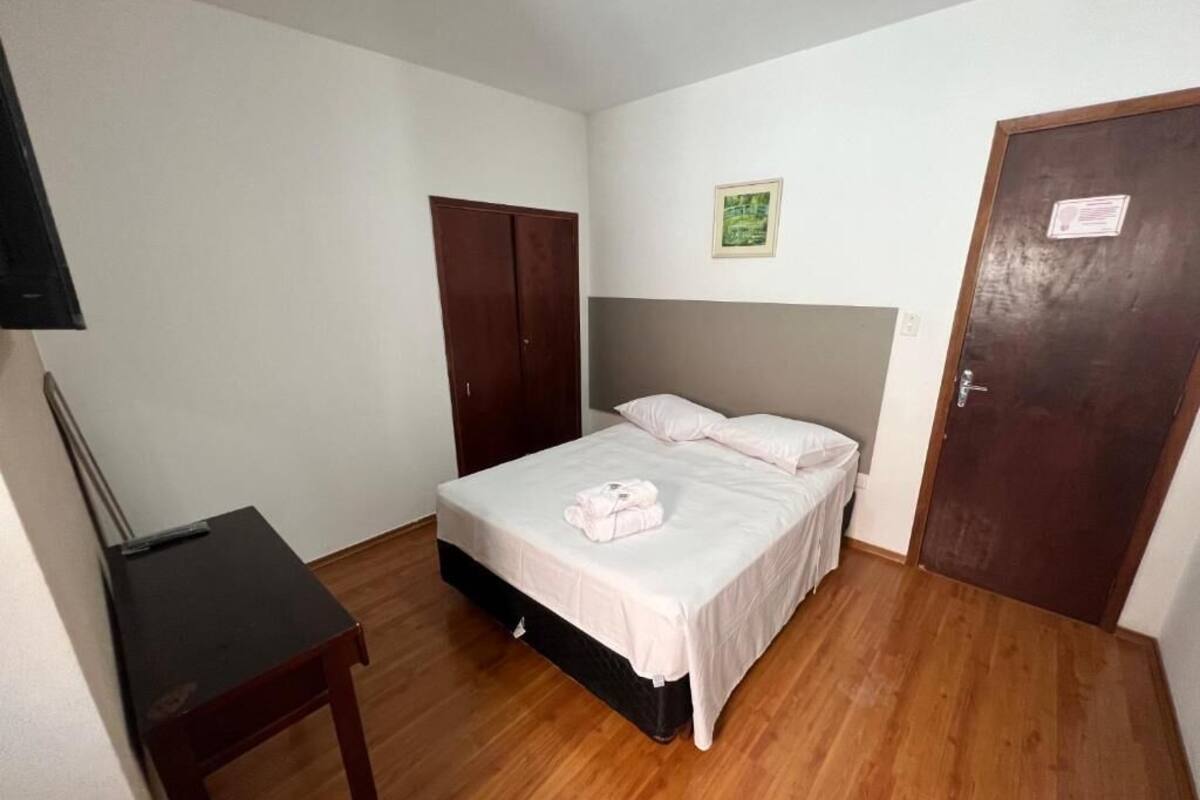 Um quarto com uma cama, guarda-roupa, escrivaninha e uma porta.