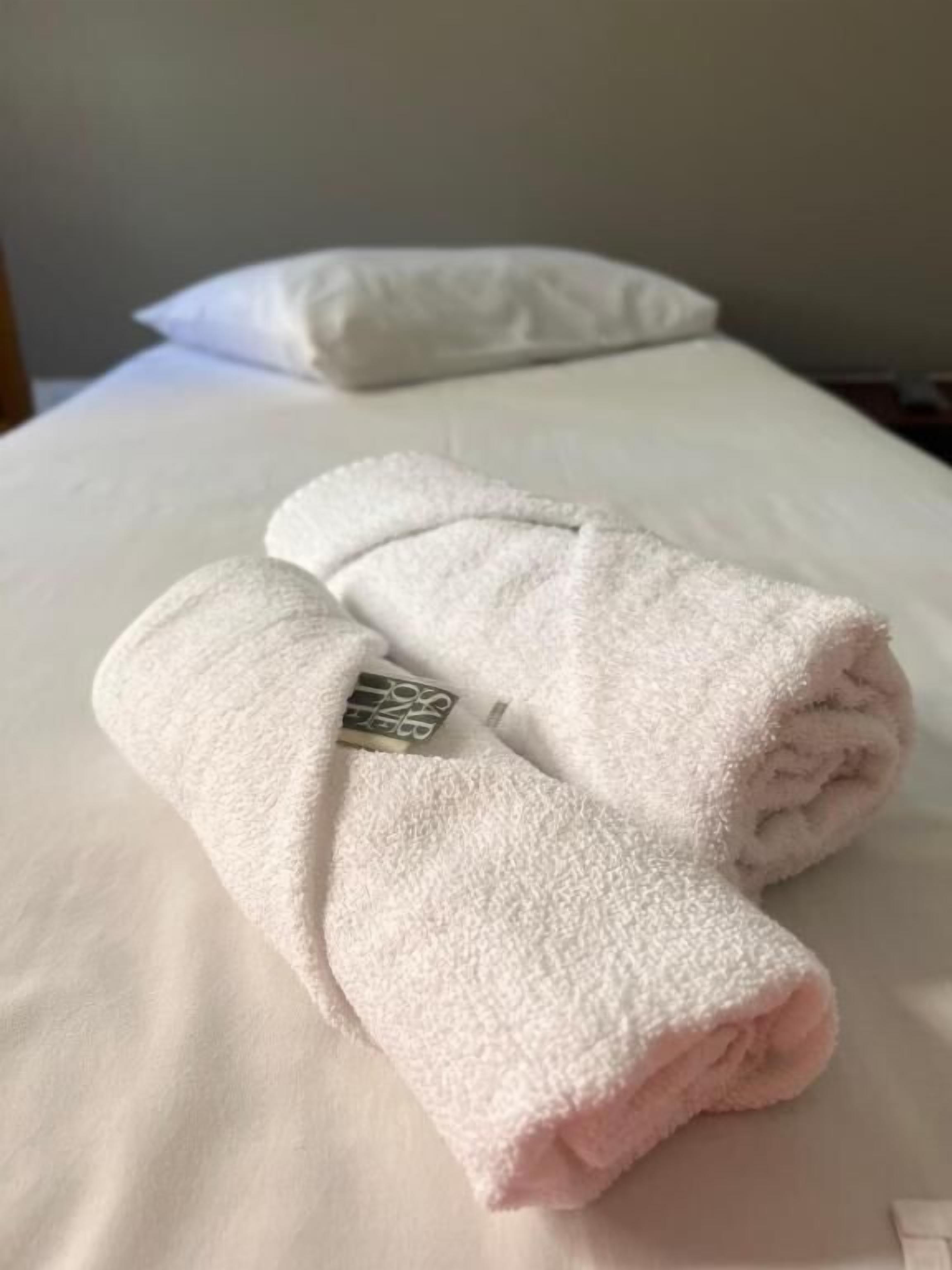 Ein ordentlich bezogenes Bett mit weißen Leinentüchern und zwei aufgerollten Handtüchern darauf.