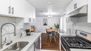 A modern kitchen with white cabinets, a stainless steel sink, a wooden dining table, and a gas stove. - Heart of DT Alhambra Walk to Starbucks Near DTLA A (Alhambra)