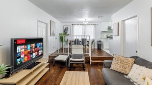 A living room with a flat-screen TV, a grey sofa, a wooden coffee table, and a dining area with a white chair and a small table. - Heart of DT Alhambra Walk to Starbucks Near DTLA A (Alhambra)