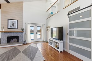 Un salón amplio con chimenea, un televisor grande y un ventanal corredero que da a un balcón.