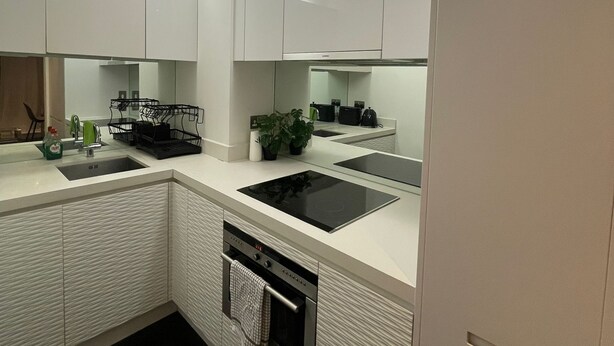 A modern kitchen with white cabinetry, a built-in oven, and a dishwasher. - Luxury Canary Wharf 1 bed apt (London)