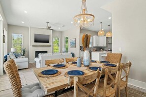 A modern kitchen with white cabinets, a dining table set with blue plates, and a chandelier. - Indigeaux - 4BR/3.5BA Blue Mountain Beach Home - Sleeps 9 - 6-Seat LSV (Santa Rosa Beach)