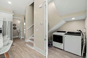 A modern kitchen with a built-in washer and dryer, a refrigerator, and a dining area with a white table and chairs. - Indigeaux - 4BR/3.5BA Blue Mountain Beach Home - Sleeps 9 - 6-Seat LSV (Santa Rosa Beach)