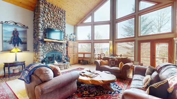 Ein gemütliches Wohnzimmer mit Kamin aus Stein, Ledersofas, einem großen Fenster und einem Bild an der Wand.