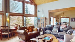 Ein geräumiges Wohnzimmer mit großen Fenstern, Ledersofas, einem Holztisch und einem Essbereich mit Stühlen und Tisch.