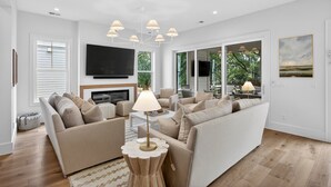 A modern living room with a sofa set, a coffee table, a TV, and a chandelier. - BRAND NEW BUILD; Gorgeous home with POOL, Hot Tub, and steps to BEACH! (Isle Of Palms)