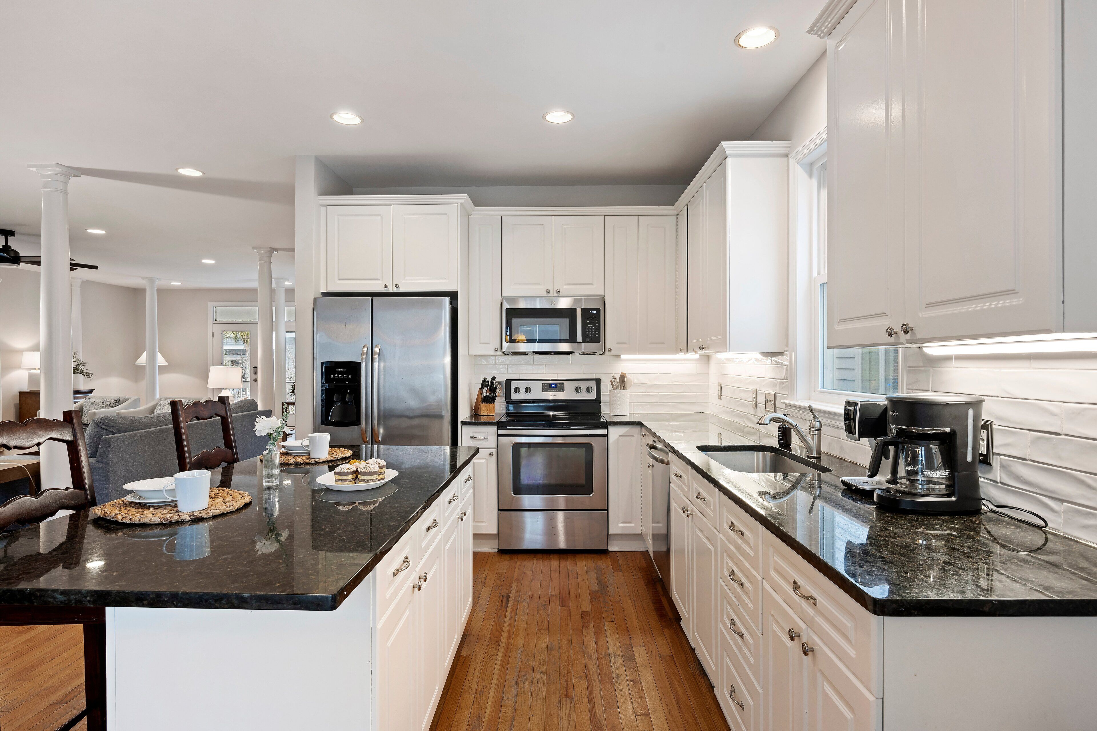 A modern kitchen with white cabinets, stainless steel appliances, and a black granite countertop.