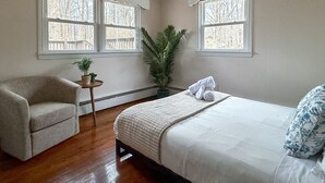 A bedroom with a bed, a chair, a small table with a plant, and a window with a view of trees. - Cozy Private Home | Near DC & Military Bases (Indian Head)