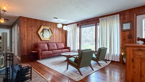 A spacious living room with a wooden floor, a red sofa, a coffee table, and two armchairs. - Cozy Private Home | Near DC & Military Bases (Indian Head)