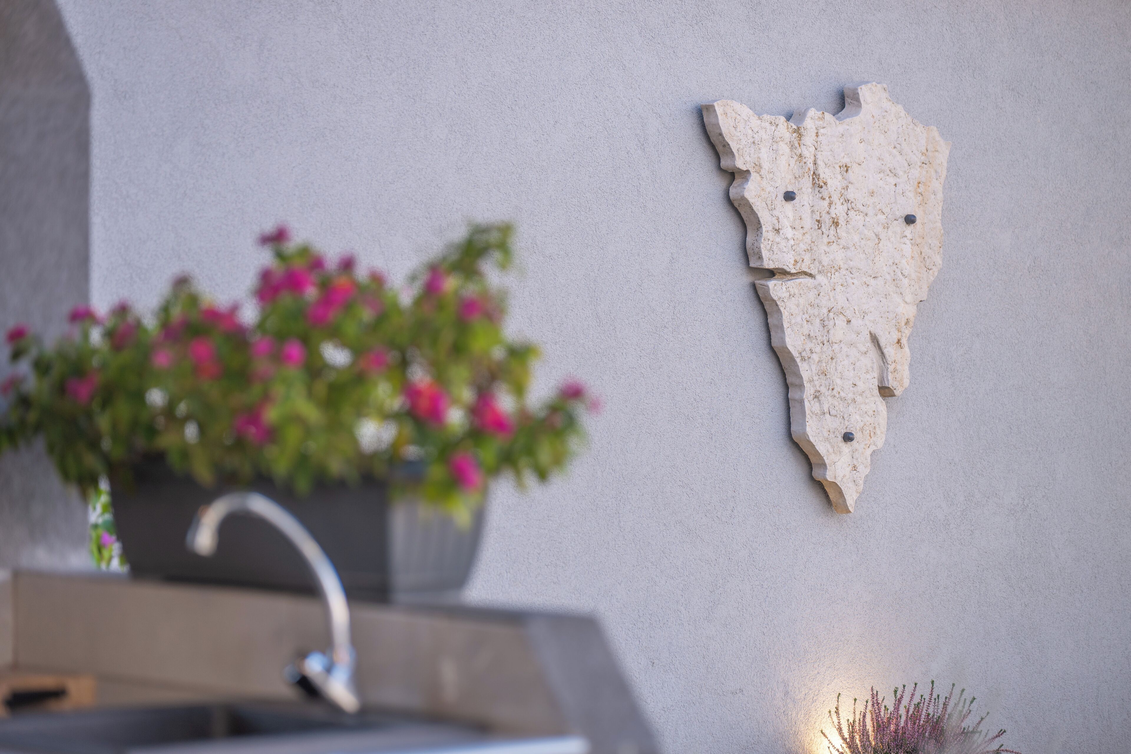 A bathroom with a sink, a decorative wall piece, and a potted plant with pink flowers.
