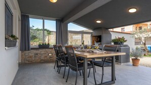 Un espace extérieur aménagé pour les repas, avec une table et des chaises, un mur en pierre et des plantes en pot.