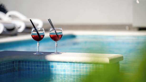 Une piscine avec deux verres remplis d’un liquide rouge, posés sur le bord.
