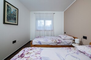 Habitación de hotel con dos camas, un cuadro en la pared, una ventana con cortinas traslúcidas y una mesita de noche con lámpara.