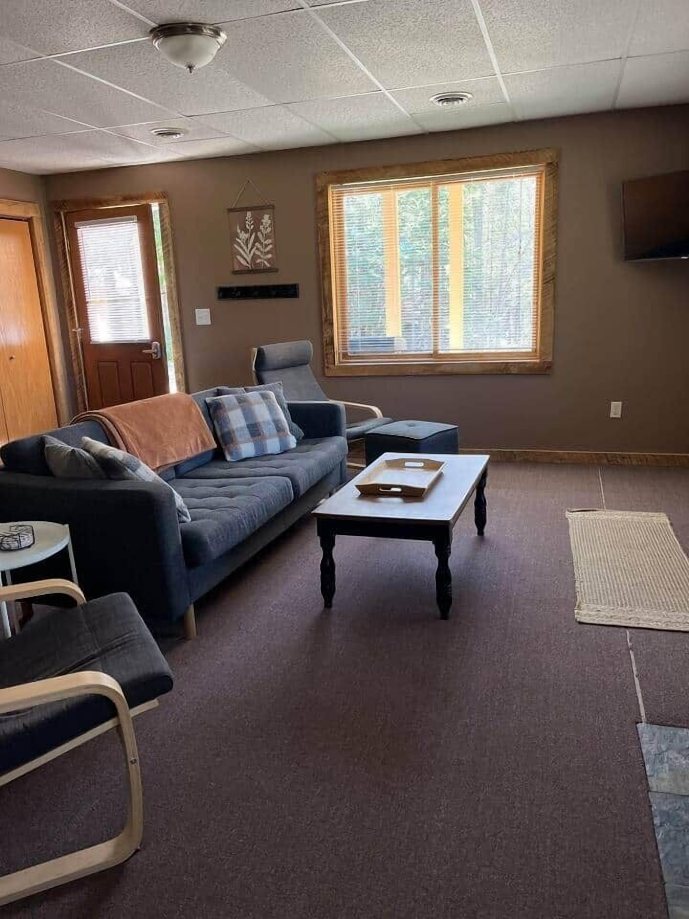 A living room with a sofa, armchair, coffee table, and a television on the wall.