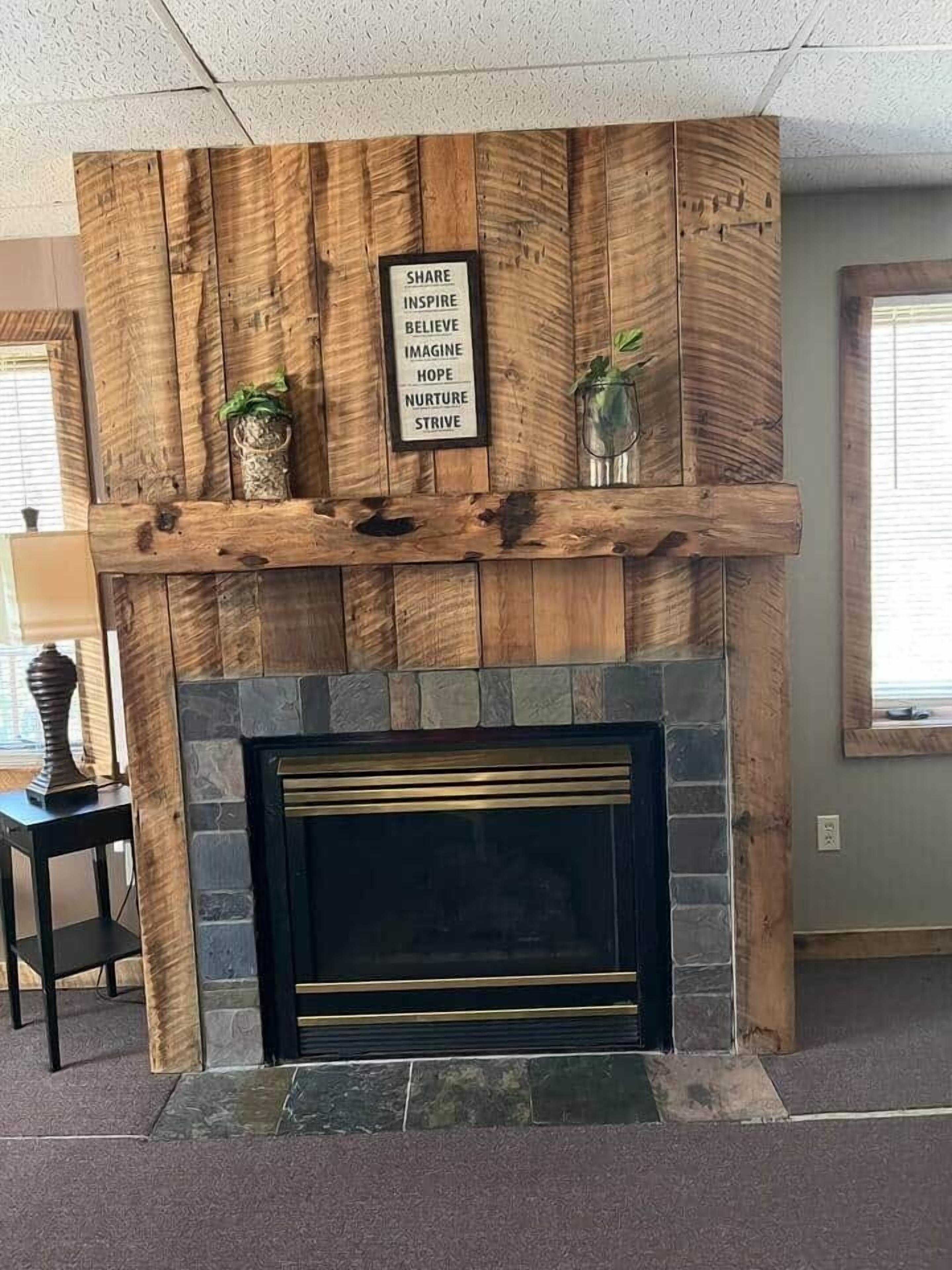 A fireplace with a wooden mantel and a motivational sign.