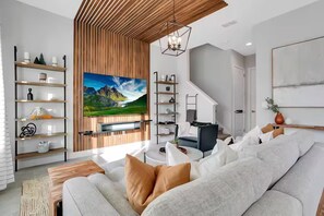 Ein modernes Wohnzimmer mit großem Flachbildfernseher, Holzregalen, einer Couch und einem Couchtisch.