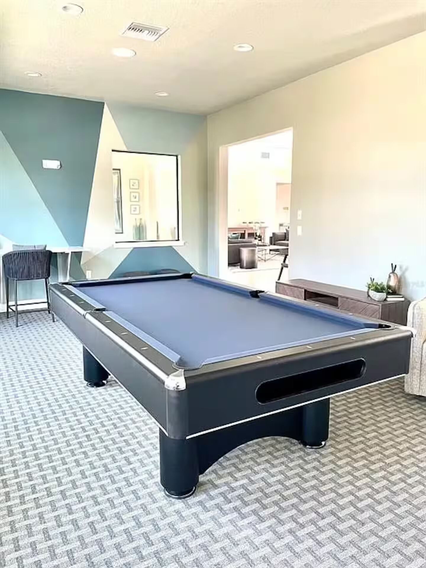 Una mesa de billar en una habitación con alfombra de diseño geométrico, una silla y un sofá.
