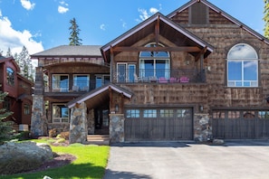 A two-story log cabin with a stone foundation, large windows, and a garage. - New! Whitefish Ski-In/Ski-Out Escape with Hot Tub & Deck! (Whitefish)