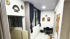 Et lille kontorrum med hvidt loft, et vindue med gardiner, et skrivebord med stol og en radiator.