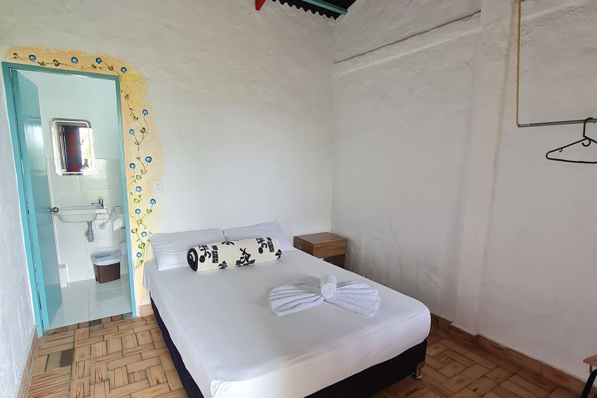 A bedroom with a bed, a wooden floor, a small bedside table, and a mirror.