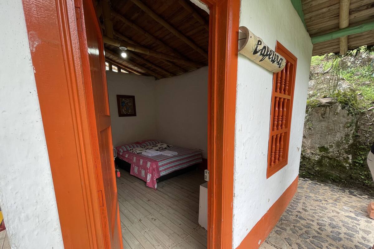 A room with a bed, a small table, and a window with a wooden shutter.
