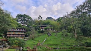A traditional multi-story building with balconies, surrounded by lush greenery and a pond. - Aldea Los Pioneros (Venecia)
