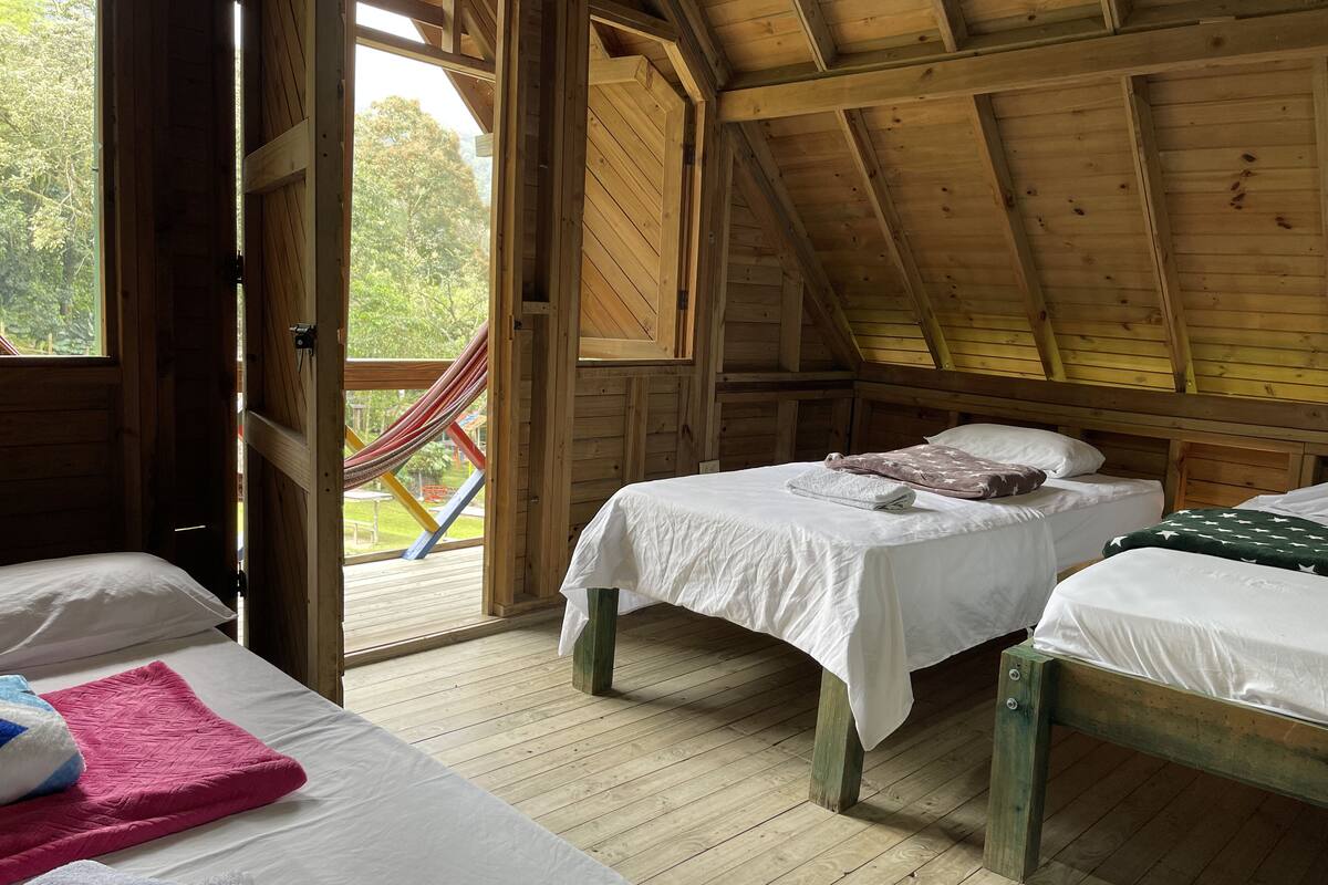 A wooden cabin with two beds, a hammock, and a view of the outdoors.