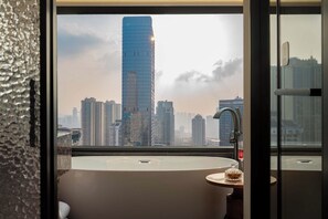 A modern bathroom with a large bathtub, a glass shower enclosure, and a view of a cityscape with tall buildings. - Joyee Sky City Hotel Chongqing-Jiefangbei (Chongqing)