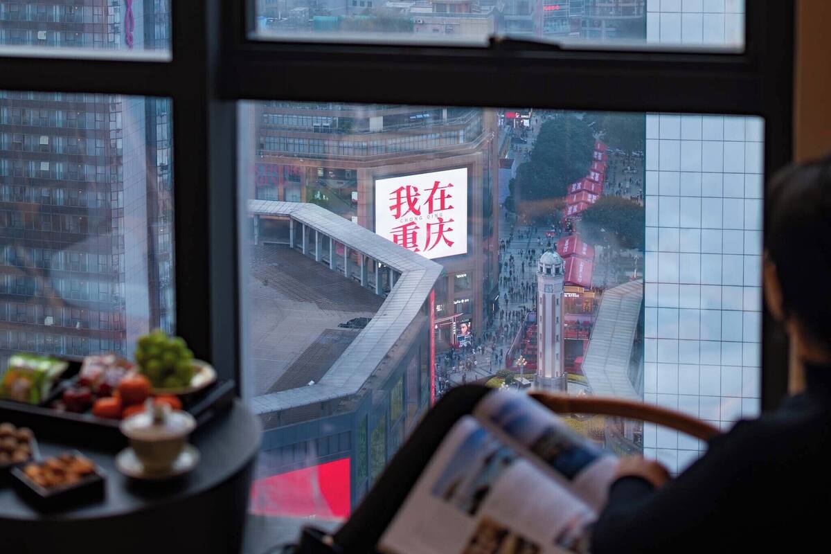 Blick aus einem Fenster, mit einer Zeitung, einem Tisch mit Snacks und einem Schild mit chinesischen Schriftzeichen.
