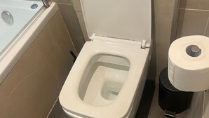 Ett badrum med en toalett, en svart soptunna och en toalettpappersrulle.