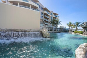 Ein Resort-Pool mit Wasserfall, umgeben von einem mehrstöckigen Gebäude mit Balkonen.