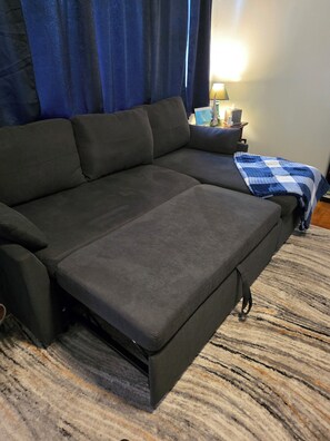 A sectional sofa with a pull-out bed in a room with a patterned carpet and a lamp on a side table. - Cozy 2-bedroom house in Haines Falls near Katterskill falls . (Haines Falls)