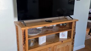 A wooden entertainment center with a flat-screen TV, a remote control, and decorative items. - Cozy 2-bedroom house in Haines Falls near Katterskill falls . (Haines Falls)