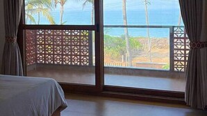 A bedroom with a bed, a large window with curtains, and a view of the ocean and palm trees. - Lahari by Hireavilla - Chic 4BR Beachfront Villa (Udupi)