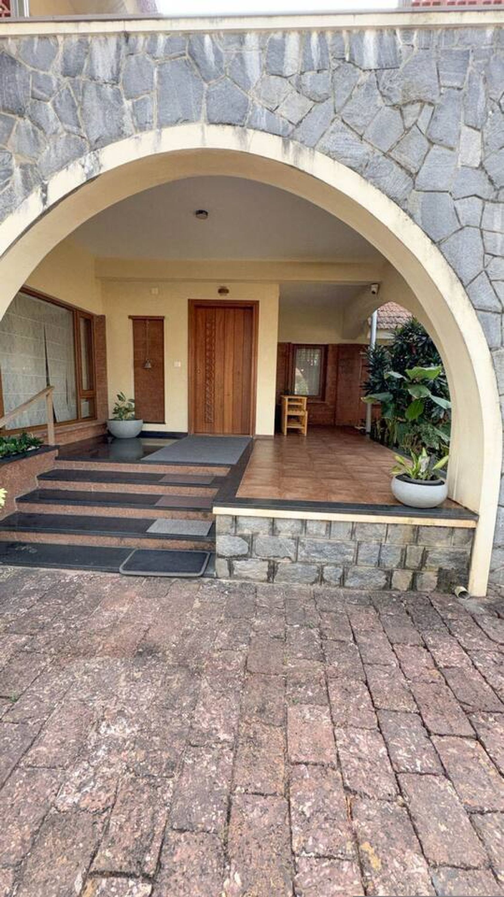 A stone archway leading to a covered entrance with a wooden door, a small table, and potted plants.