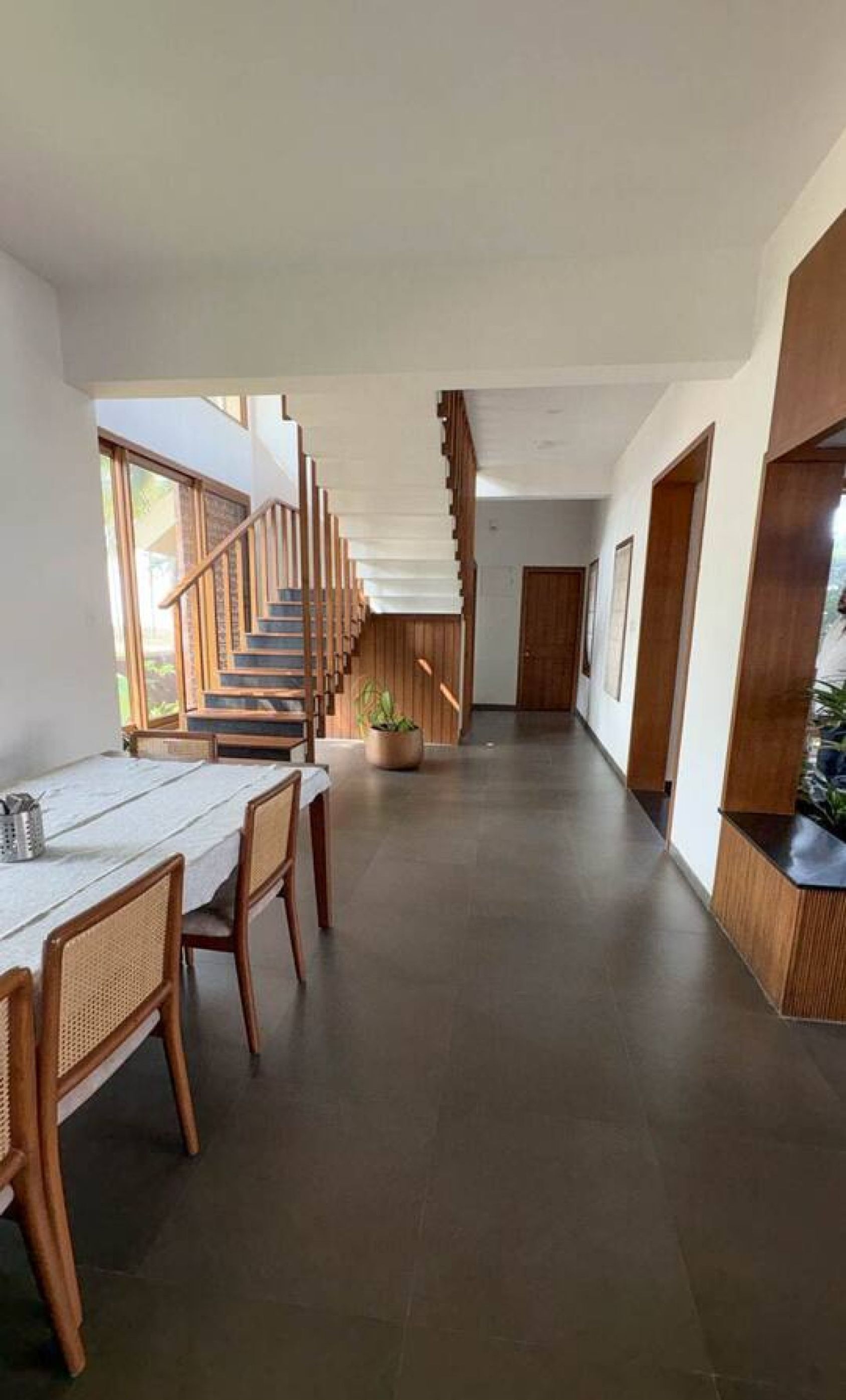A modern interior with a staircase leading to upper floors, a dining area with a table and chairs, and a potted plant.