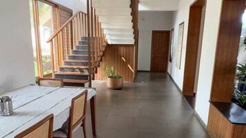 A modern interior with a staircase leading to upper floors, a dining area with a table and chairs, and a potted plant.