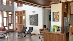 A spacious living area with a wooden ceiling, a kitchen with a refrigerator, and a dining area with chairs and a table. - Lahari by Hireavilla - Chic 4BR Beachfront Villa (Udupi)