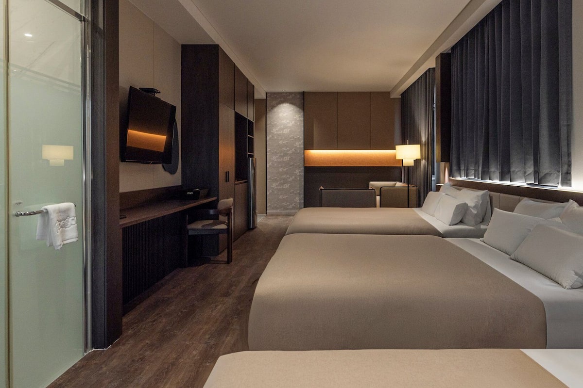 A hotel room with two beds, a TV, a desk, and a bathroom.