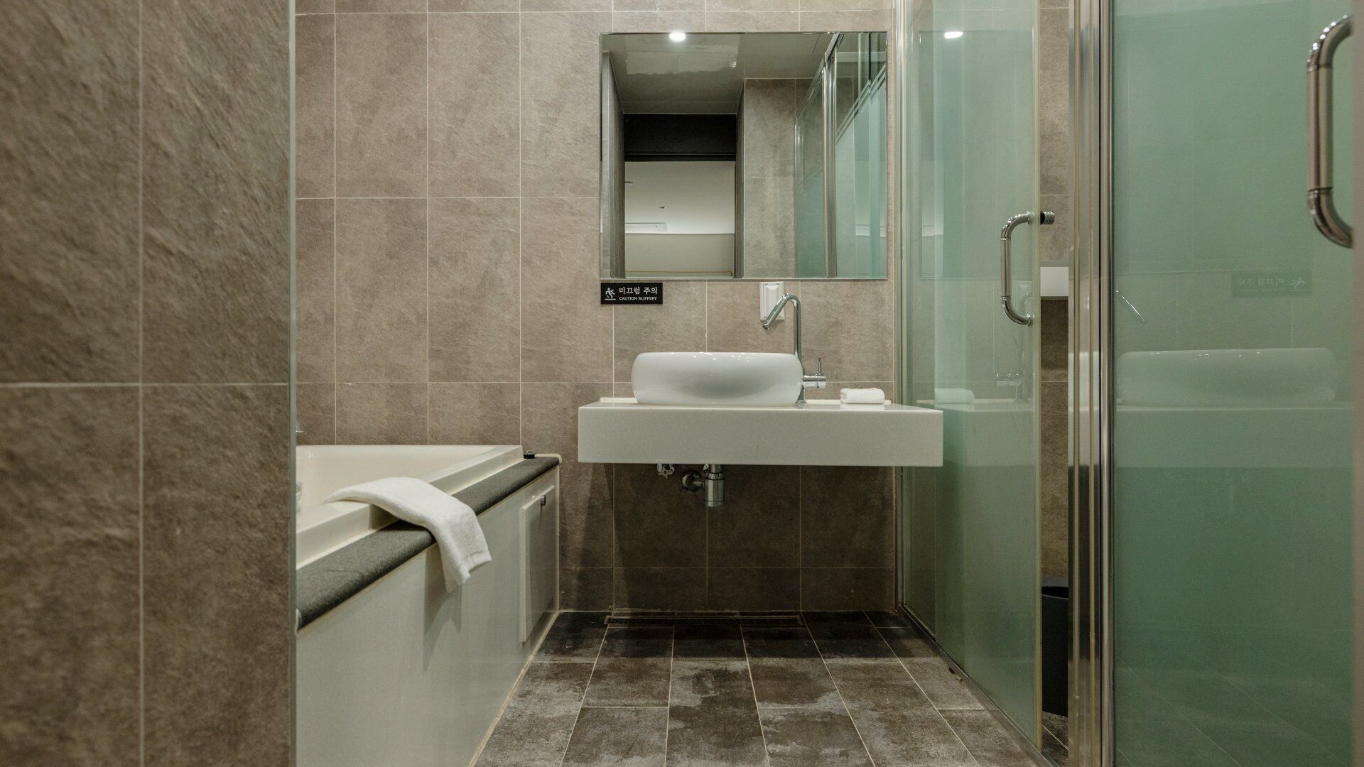 A modern bathroom with a glass shower enclosure, a sink with a mirror above it, and a towel on the edge of the bathtub.