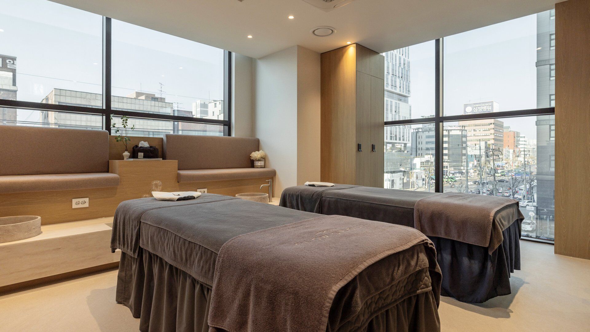 A modern spa room with two massage tables, a sofa, and a view of the city.