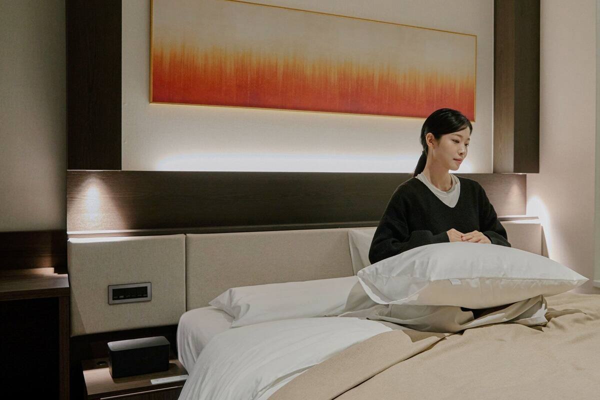 A hotel room with a bed, a nightstand, a wall-mounted control panel, and a large abstract painting.