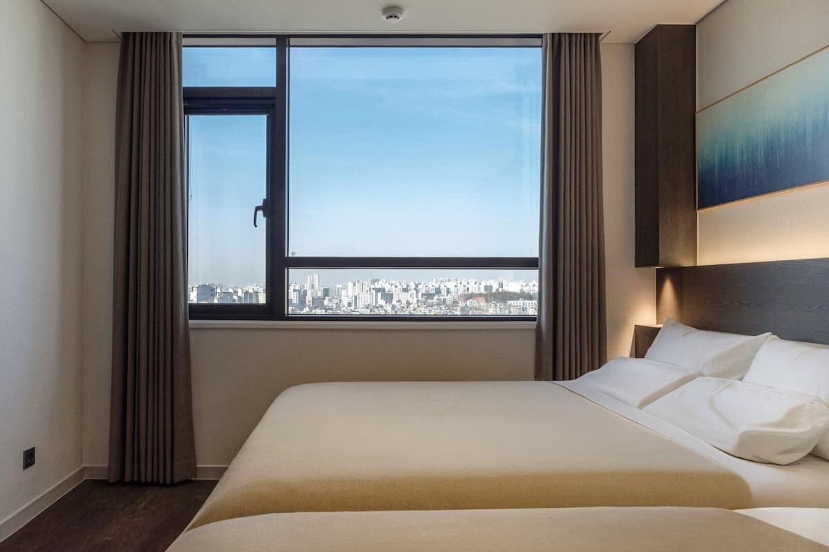 A hotel room with a bed, a window with curtains, a city view, and a mounted television.
