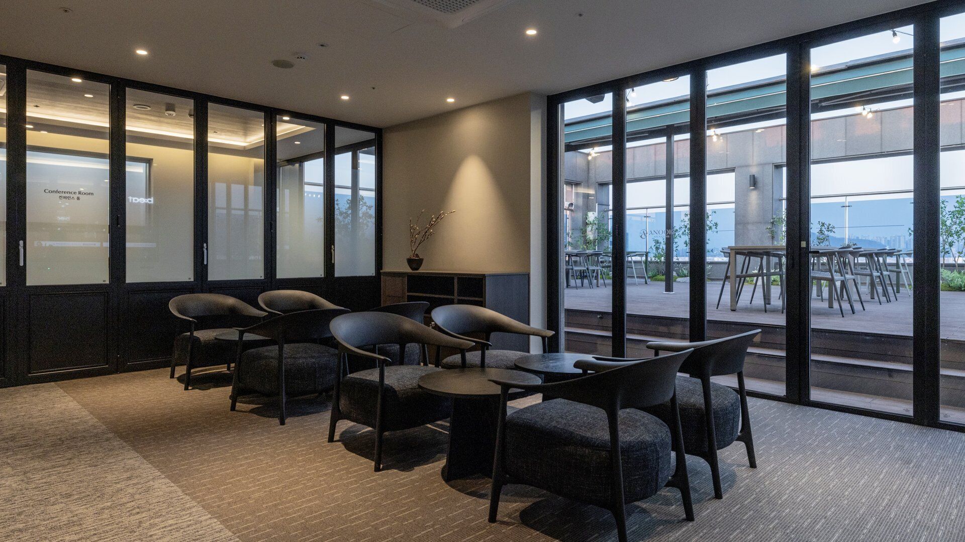 A conference room with modern chairs and tables, large windows, and a view of the outdoors.